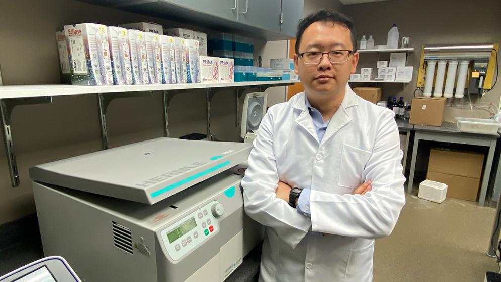 Jingxin Wang stands next to instruments in the lab
